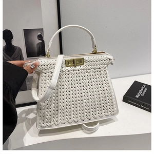 Detailed view of white woven handbag with golden turn-lock closure and leather top handle
