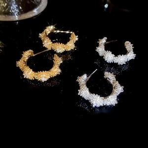 Macro shot of gold and silver C-shaped floral earrings with sparkling zircon crystal texture