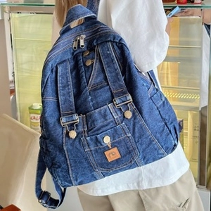 Detail of denim tote bag with layered pockets, metal zippers and brown leather patch
