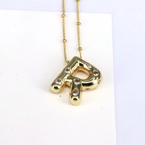 Macro detail of 18k gold R-letter bubble pendant with cubic zirconia on dudu chain