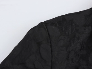 Detailed macro view of black jacquard fabric texture on the wide-shoulder coat sleeve