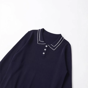 Flat lay of navy knit polo shirt with white wavy trim and long sleeves on white background