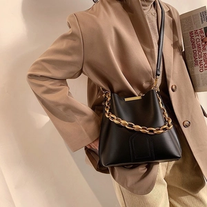 Minimalist black leather bucket bag with gold chain strap on a model, classic retro style