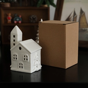White ceramic Christmas house ornament with original brown gift box on warm wooden shelf