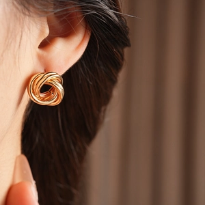Gros plan de boucles d'oreilles nœuds dorées portées par un mannequin sur fond de tissu