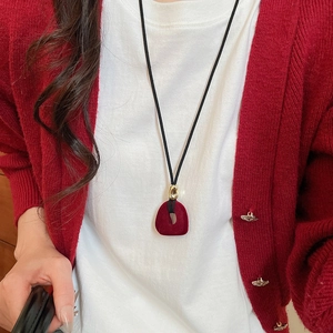 Detail of red flocked geometric pendant on black cord worn over red knit cardigan