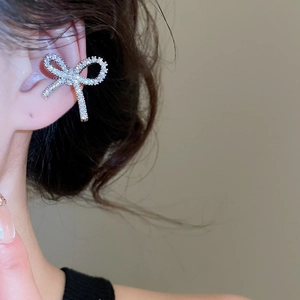 Detail of silver bow ear cuff with pavé crystals worn on the upper ear cartilage