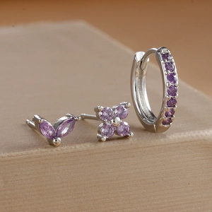 Detailed macro view of silver flower and butterfly stud earrings set with purple stones