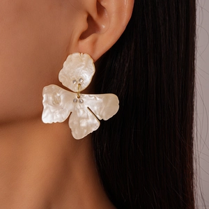 Close-up of white resin flower earring with rhinestones worn by a model in a studio