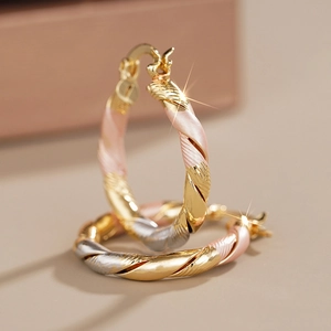Macro shot of stylish tri-color twisted hoop earrings with gold, rose gold, and silver finish