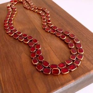 Detailed close-up of double-layer necklace with red glass beads and gold metal settings