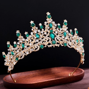 Close-up of golden crown featuring green and clear crystals on a dark wooden tray