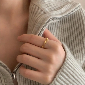Detail of a minimalist gold hollow heart ring worn on a finger against a knit sweater