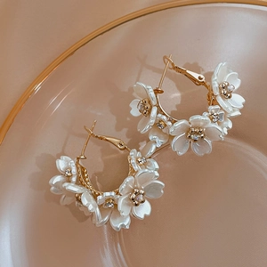 Macro detail of gold-plated flower hoop earrings with white acrylic petals and crystal centers