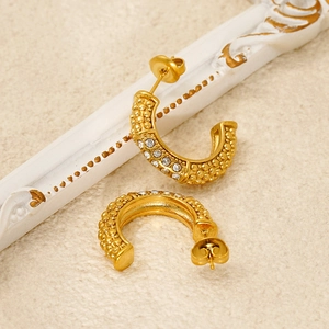 Macro detail of gold-plated U-shaped earrings with textured relief and inlaid crystals