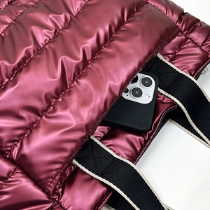 Detail of burgundy quilted puffer bag showing glossy metallic texture and phone storage
