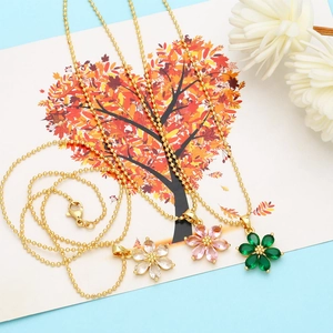 Detail of three floral pendant necklaces in white, pink, and green with gold bead chains