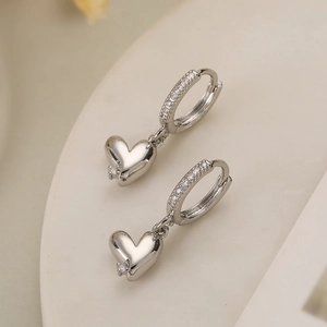 Detail of silver heart hoop earrings with cubic zirconia inlay on a beige stand