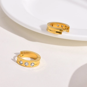 Detail of wide gold-plated huggie hoop earrings with three inlaid white cubic zirconias
