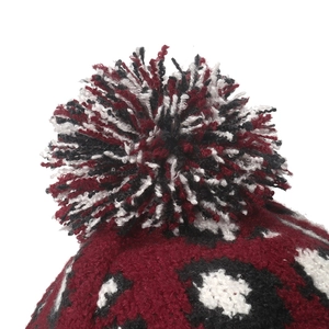 Détail du bonnet en tricot léopard rouge et noir avec un gros pompon en laine mélangée