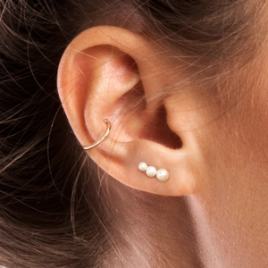 Close-up of gold ear cuff and minimalist triple pearl stud earrings on model's ear