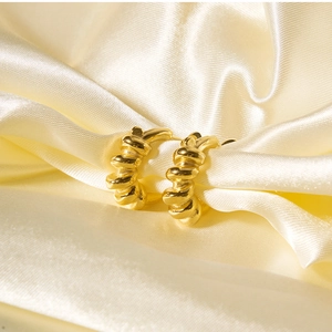 Detail of gold twisted rope texture earrings on luxurious yellow silk fabric