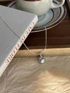 Macro shot of a grey pearl pendant on a thin silver snake chain over a book decor