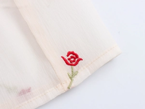 Detailed macro view of delicate red floral embroidery on off-white textured fabric