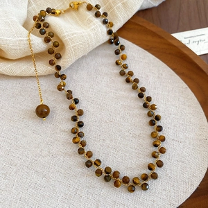 Collana di perle occhio di tigre con ciondolo a sfera dorata su vassoio in legno vintage