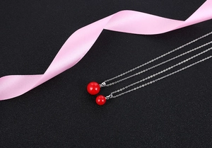 Macro detail of vibrant red shell pearl pendants with minimalist silver chains on black surface