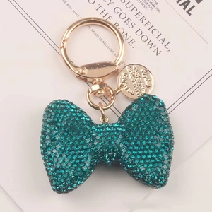 Portachiavi con fiocco in strass blu pavone e finiture dorate su sfondo minimalista