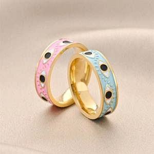 Golden evil eye rings with pink and blue enamel inlay on beige silk background