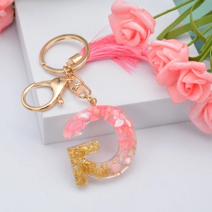 Detail of pink resin letter G keychain with gold foil flakes and a soft tassel charm