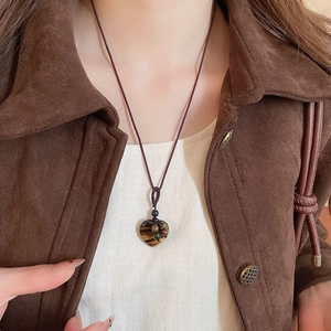Detail of tiger eye stone heart pendant on dark brown braided cord with autumn outfit