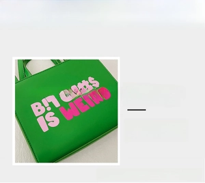 Detail of green tote bag with pink artistic lettering and smooth leather texture