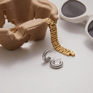 Dettaglio degli orecchini a C argentati testurizzati e del bracciale a maglie dorate su vassoio