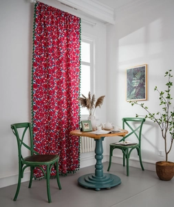 Detail of red floral cotton curtains featuring green tassel trim in a bright home setting