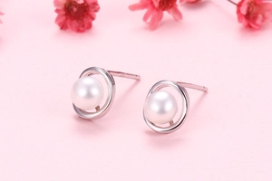 Close-up of small round white freshwater pearl stud earrings with silver pins on pink background