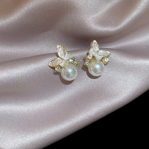 Detailed close-up of golden butterfly earrings with white pearls and sparkling rhinestones