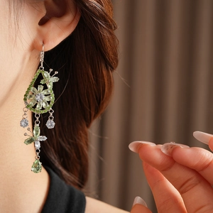 Close-up of a silver tassel earring with green and white crystals on a female model