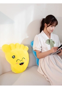 Close-up of soft yellow plush foot-shaped pillow with cartoon smile in home setting