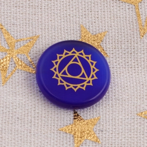 Macro di una pietra da meditazione in opale blu scuro con simbolo chakra Ajna dorato