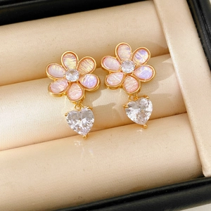 Close-up of gold floral earrings with pink resin petals and sparkling heart zircon drop