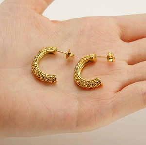 Detailed macro view of gold C-shaped earrings with textured surface and rhinestones