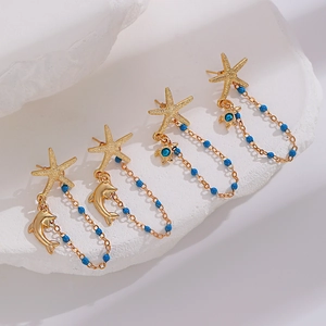 Detailed view of gold starfish earrings with blue beads and dangling sea turtle charms