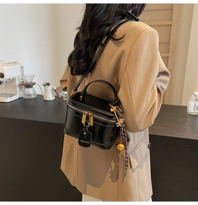 Detail of a matte black box bag with gold hardware worn by a model in a cafe