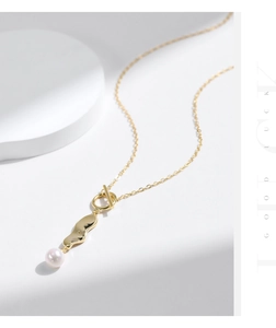 Close-up of golden pearl necklace featuring a unique wavy pendant and toggle clasp