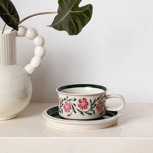 Detailed view of a vintage floral ceramic coffee cup and saucer set on a beige surface