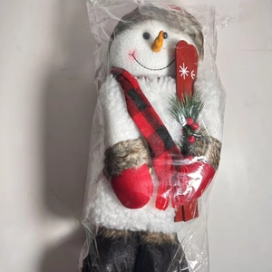 Detailed view of standing snowman plush with red black plaid scarf in transparent packaging