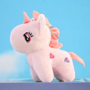 Pink plush unicorn keychain with embroidered heart details against a blue sky background